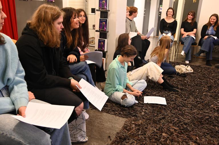 En grupp ungdomar sitter i ring och läser text