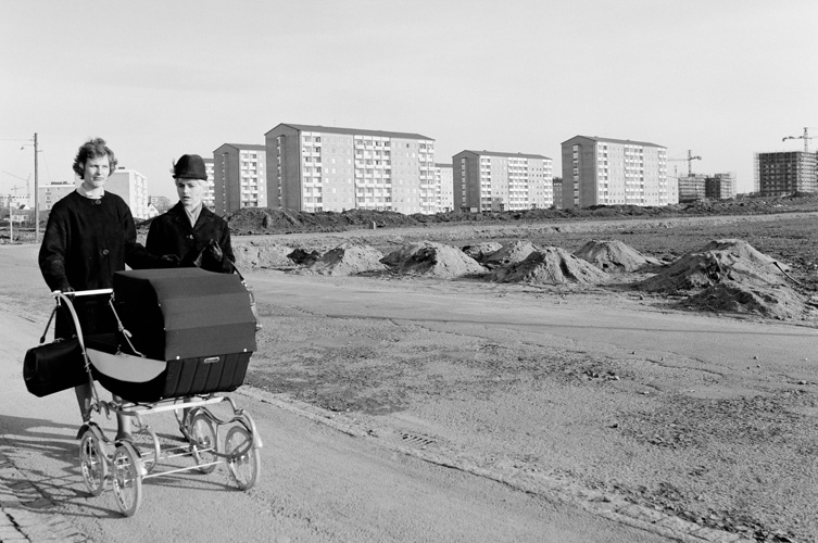 Svart vit bild på två kvinnor går med en barnvagn bland nybyggda flervåningshus