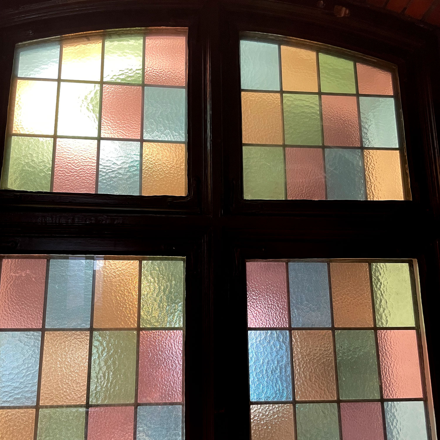 Äldre fönster med glas i olika färger som är sammanfogat med svart fönsterkit.