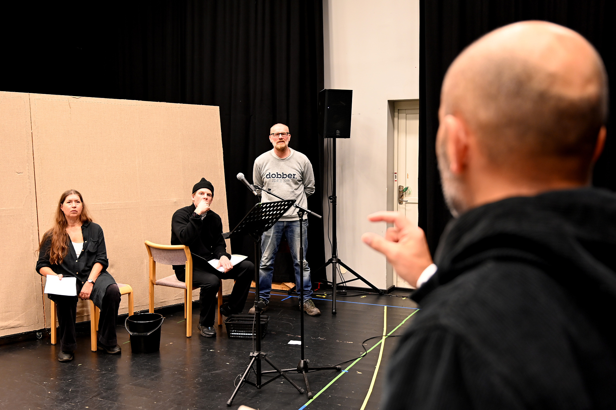 Tre skådespelare sitter och lyssnar på en person i förgrunden som ger instruktioner.