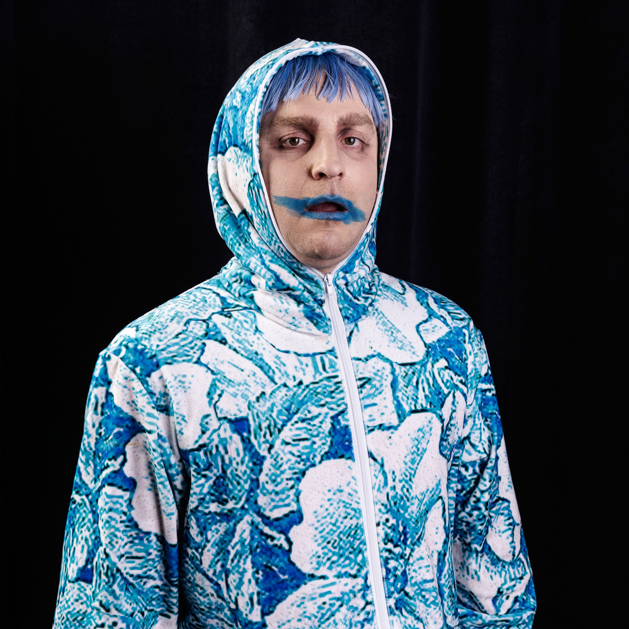En person i en blå- och vitmönstrad jumpsuit med matchande blått hår och en blåmålad mun.