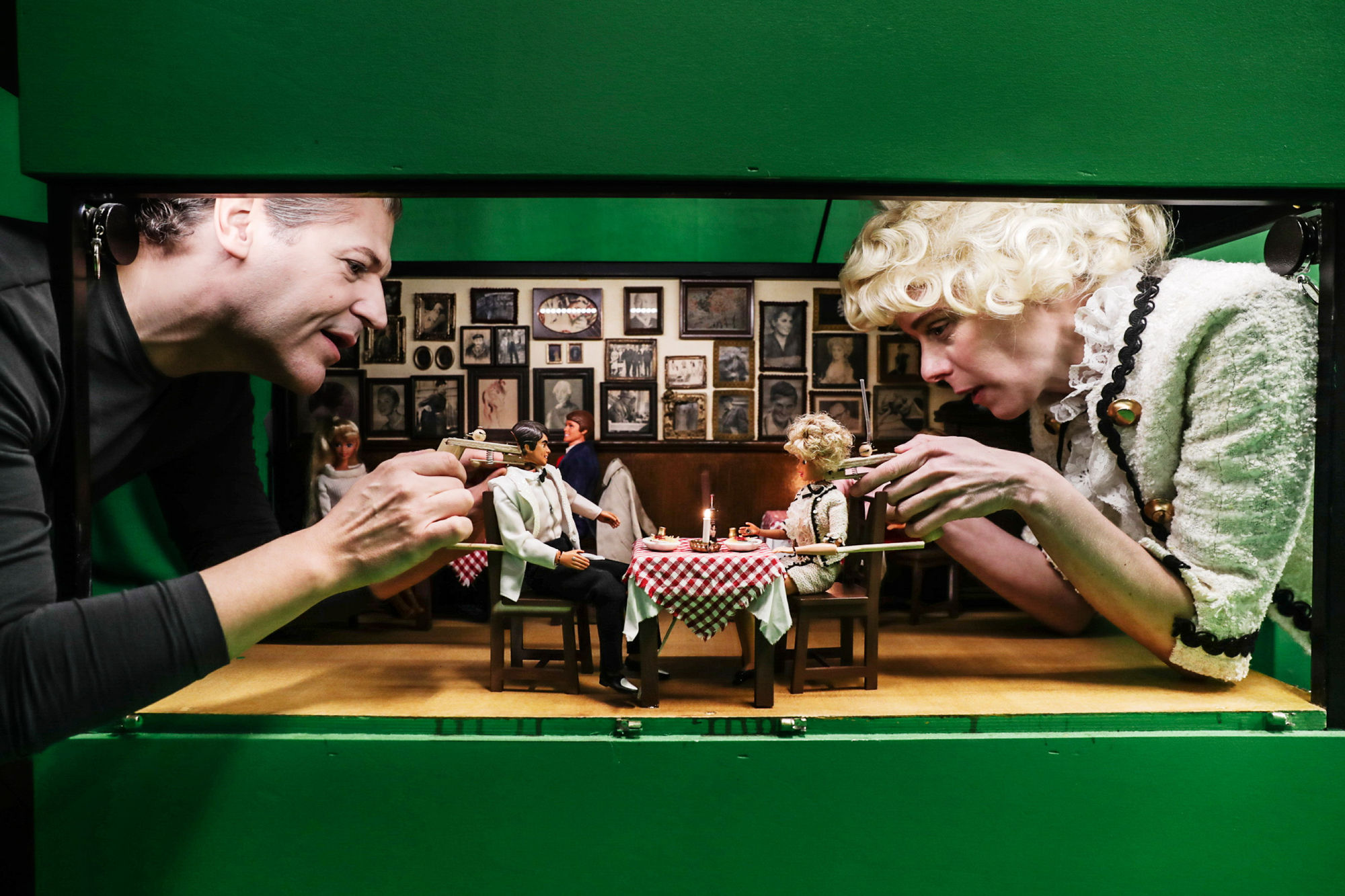 En person vid varje sida om ett dockhus. De spelar med barbiedockor.