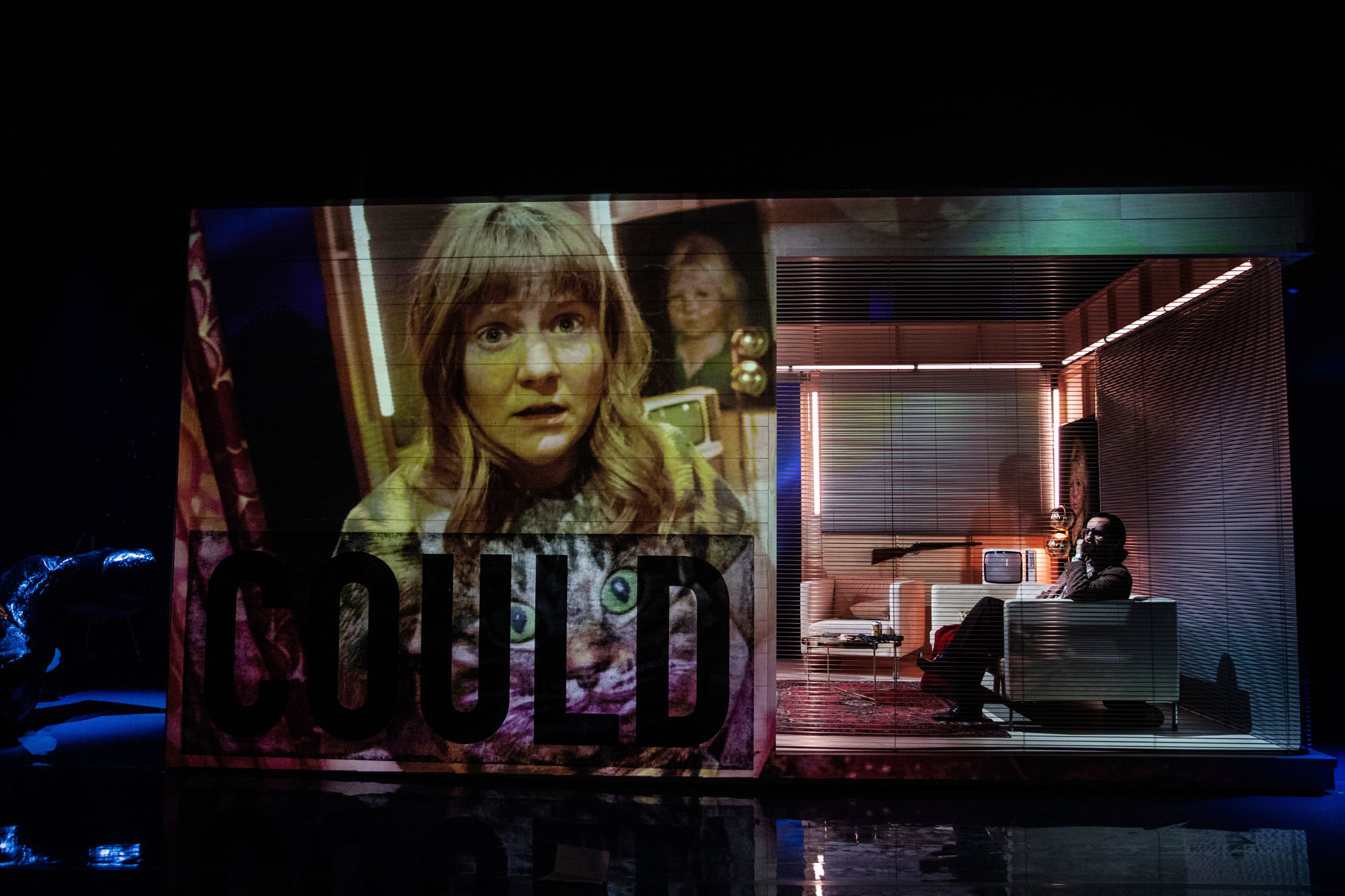 Projicering av en flickas ansikte på scenografin som är ett hus på scenen. Till höger en man i en soffa.