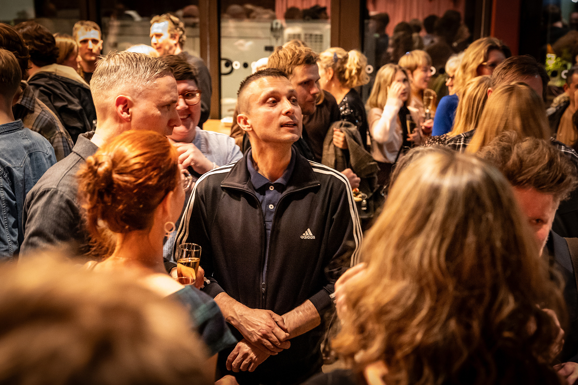 En man i en marinblå Adidas-tröja står mitt i en folkmassa och ser uppmärksamt omkring sig.