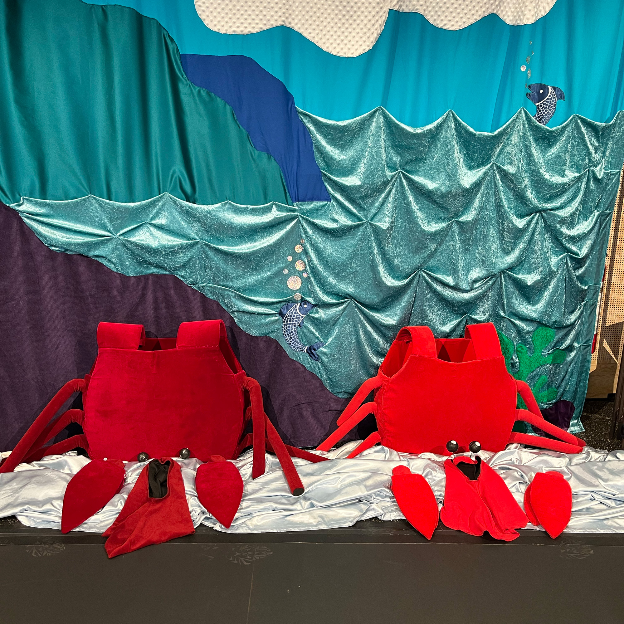 Två kostymer som liknar krabbskal, klor och mössor med spröt står på golvet mot en fond av olika blå nyanser