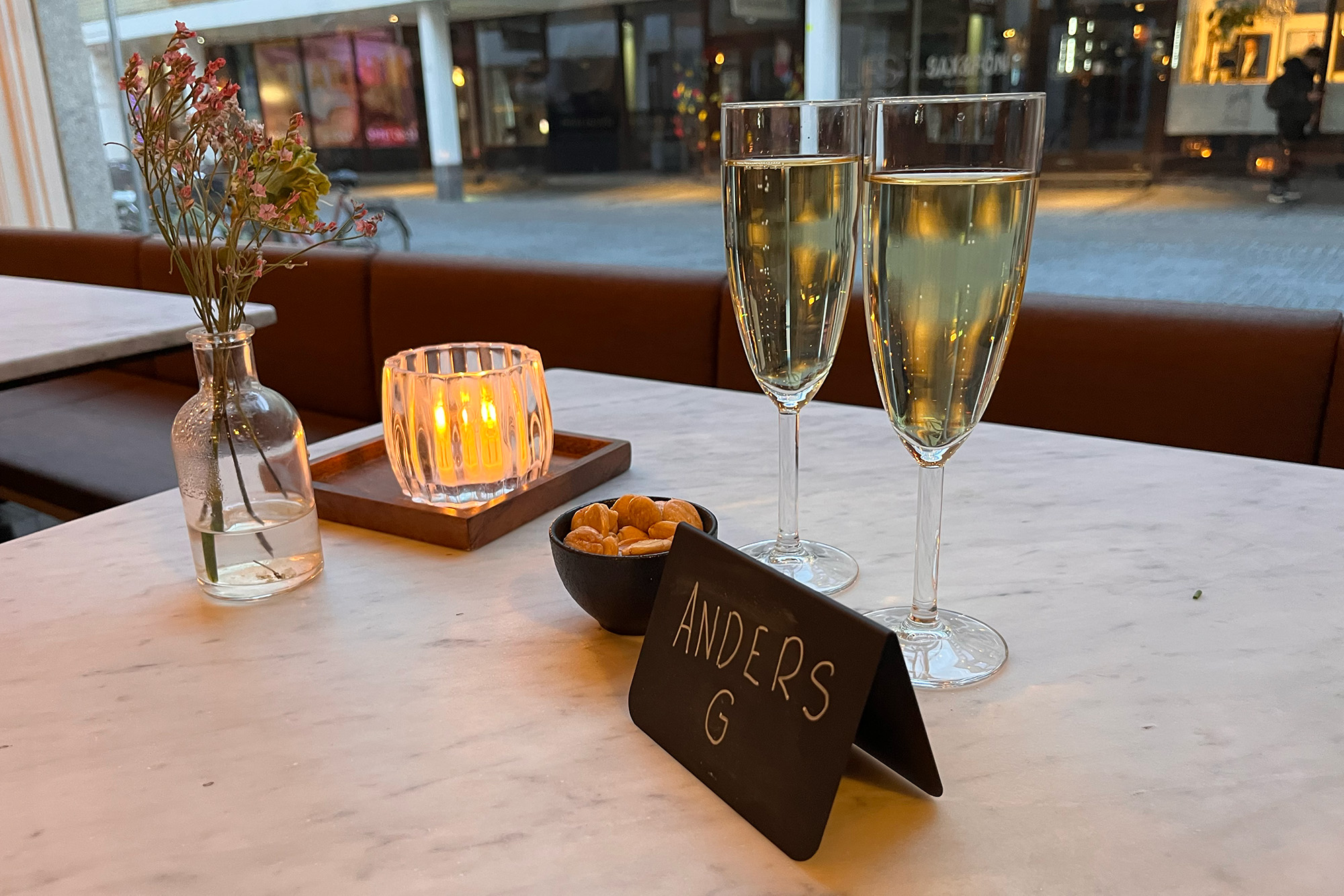 Två bubbelglas, en skål med mandlar och en namnskylt står på ett marmorbord. 