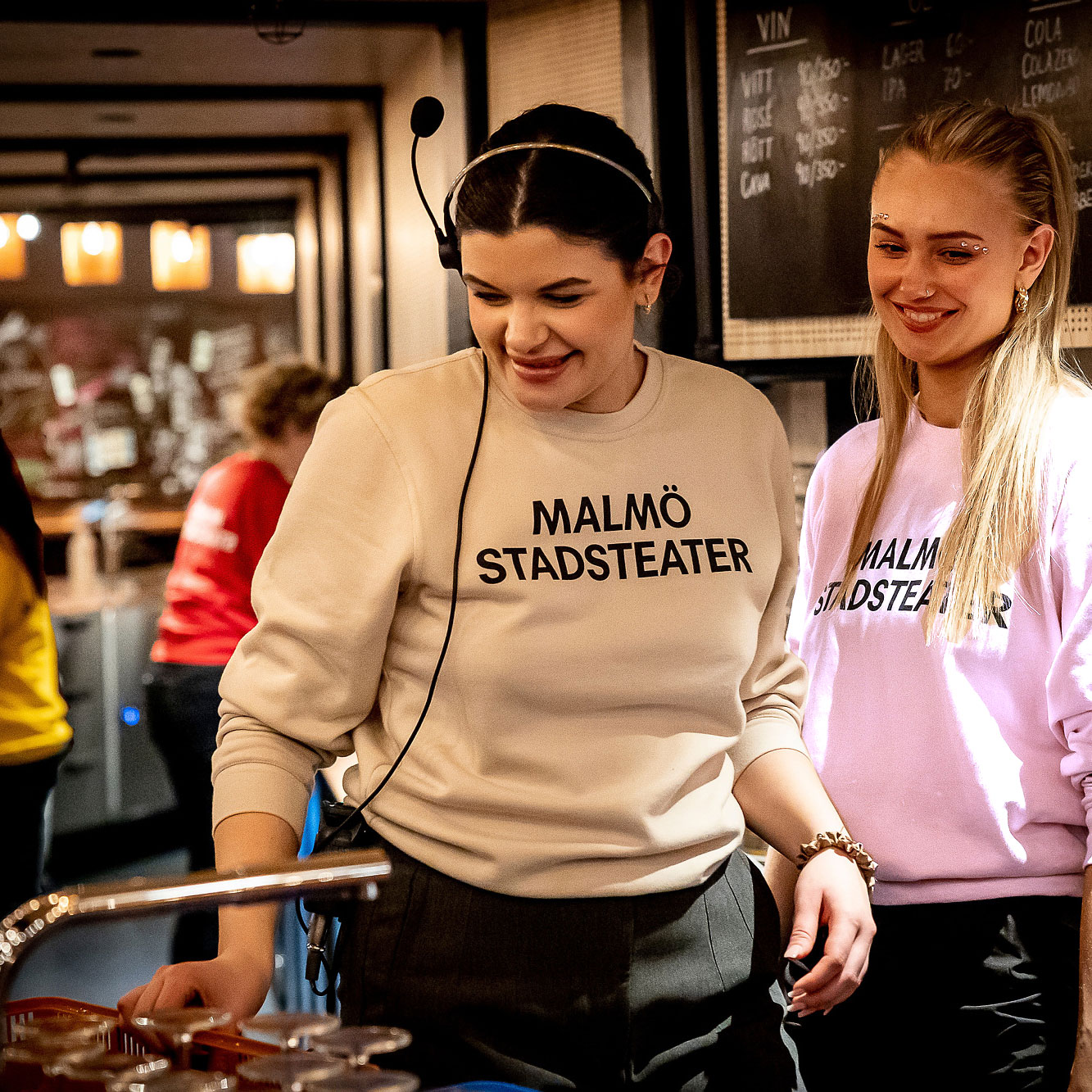 Teaterpersonal står i baren i foajén i tröjor i olika färger med Malmö Stadsteater tryckt över bröstet.