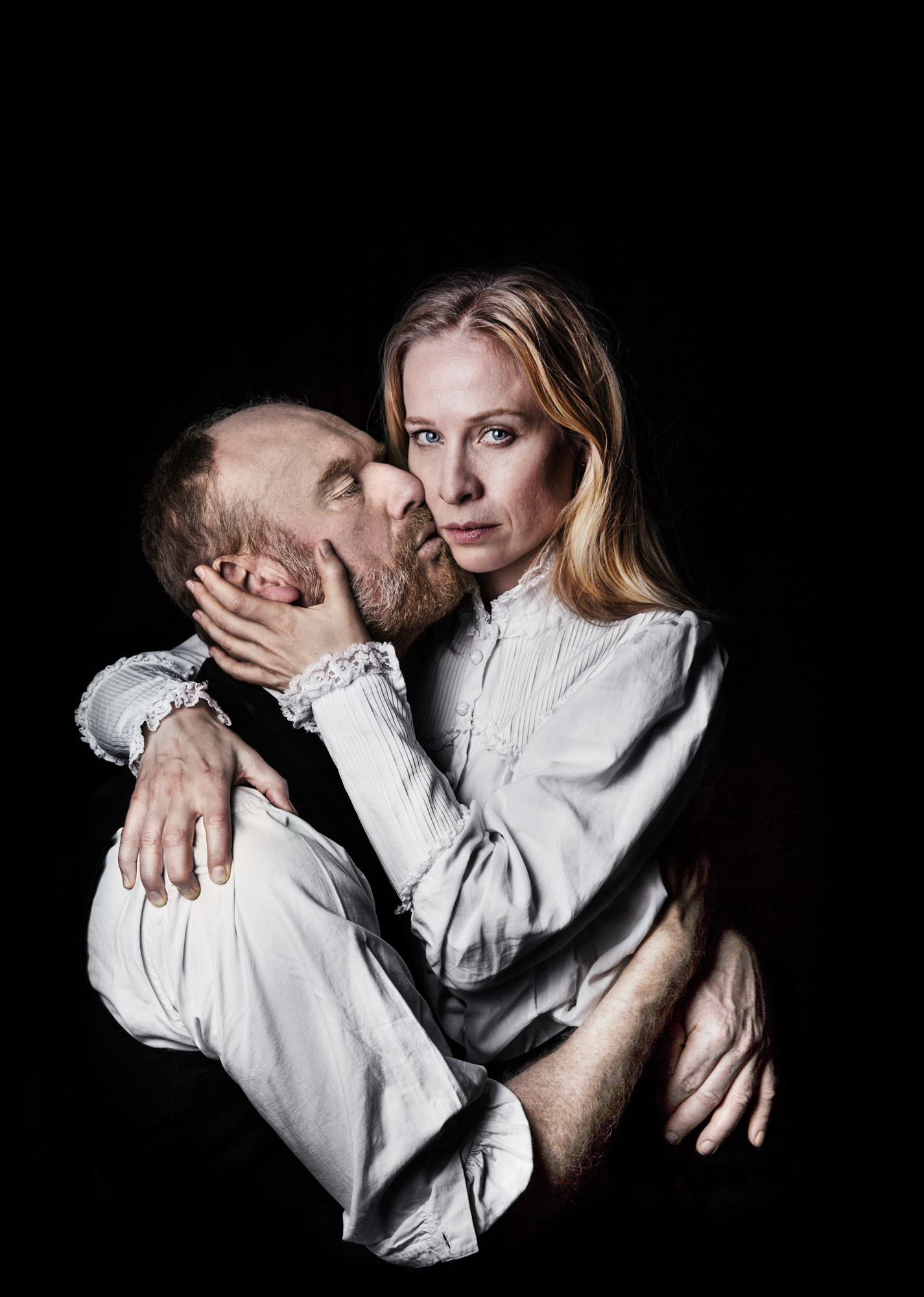 En man blundar och håller om och kysser en kvinna på kinden. Kvinnan håller om mannen tittar mot kameran.