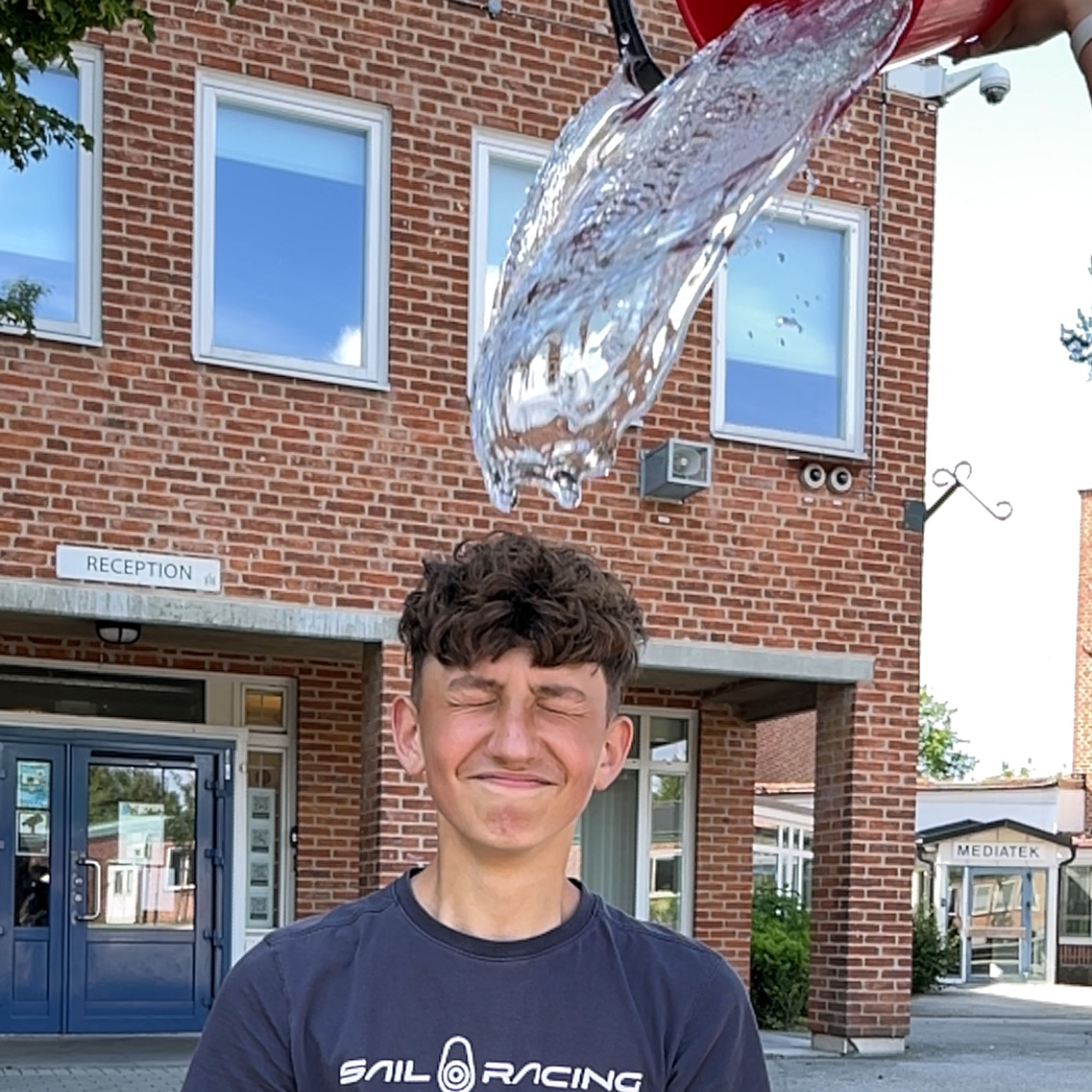 En person blundar starkt, ovanför ser vi vatten vara på väg att hällas över huvudet med en hink