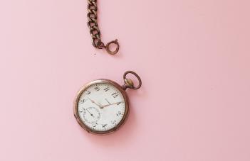 gammeldags klocka med kedja mot rosa bakgrund