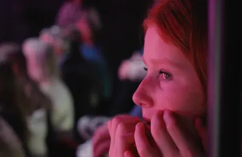 Person sitter i teatersalong, mörker och tittar koncentrerat framåt. 