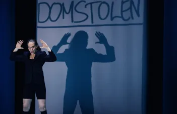 Skådespelaren står med upphöjda händer som syns som en större skugga i fonden.