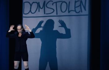 Skådespelaren står med upphöjda händer som syns som en större skugga i fonden.