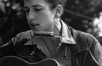 En ung Bob Dylan med akustisk gitarr och munspel 