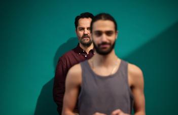 Två män står bakom varandra. Han längst bak syns skarpast.