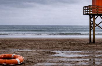 Bild på öde strand med en livboj och badvaktstorn