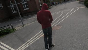 Foto Unga Malmö Stadsteater Person syns bakifrån på skolgård. Har på sig en hoodie med luva över huvudet.