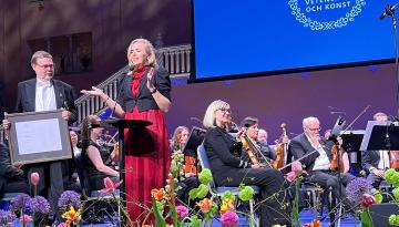 Foto Privat Prisutdelning på en scen. Två personer på förscenen. Orkester i bakgrunden.