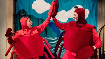 Två personer i krabbkostymer: röda overaller med krabbskal, röda mössor med antenner och krabbklor på händerna. Gör high five