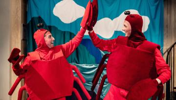 Två personer i krabbkostymer: röda overaller med krabbskal, röda mössor med antenner och krabbklor på händerna. Gör high five