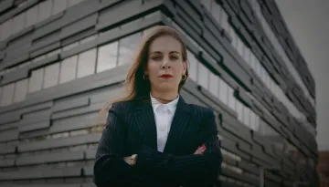 Kvinna med korslagda armar framför ett hus