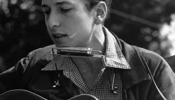 En ung Bob Dylan med akustisk gitarr och munspel 