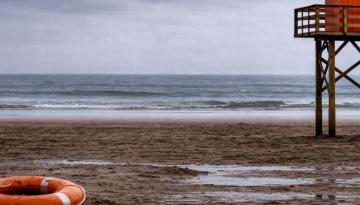 Bild på öde strand med en livboj och badvaktstorn