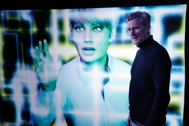 Skådespelare framför en stor skärm där AI framträder genom ljusmönster av ljus