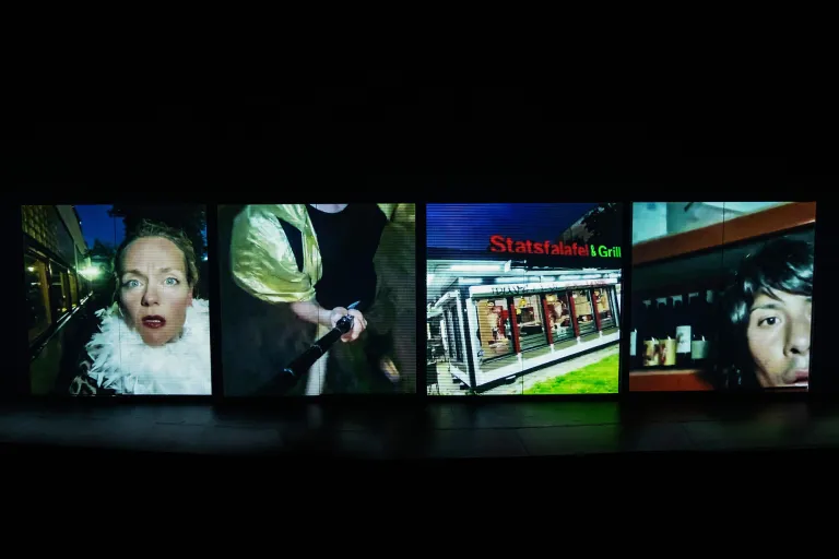 Fyra skärmar på scenen visar skådespelare ute på stan