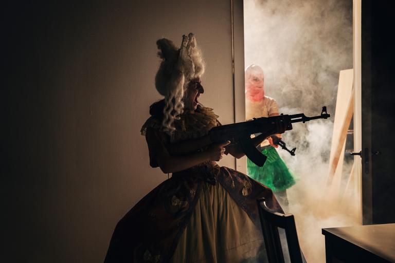 En kvinna i 1700-tals klänning skjuter med ett automatvapen