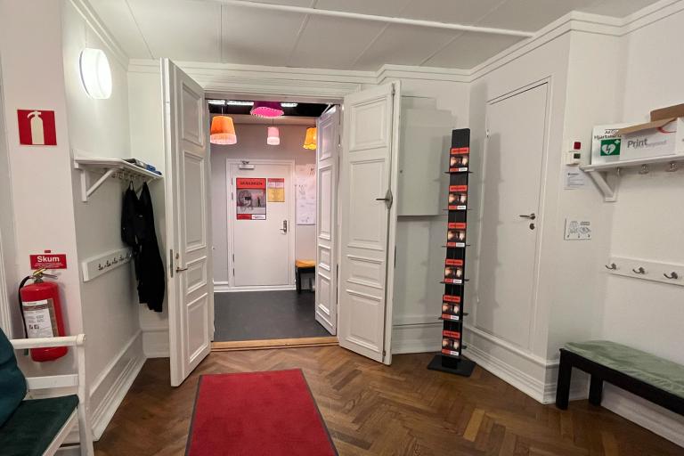 Foajé Studion. Vitt kapprum, krokar på väggarna, fiskbensparkett, bänkar längs med väggarna med dynor i olika färger