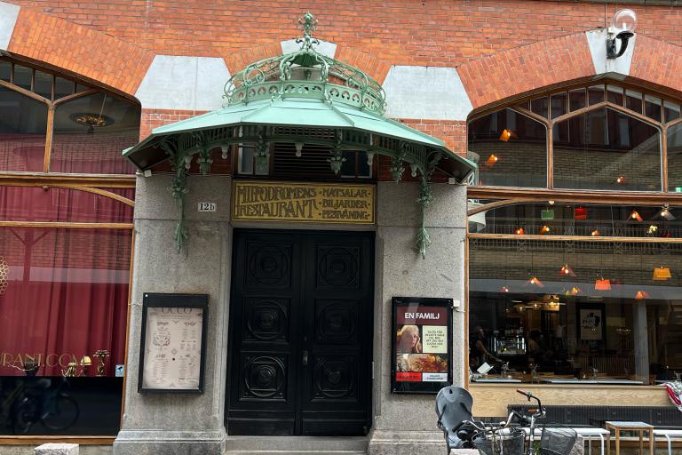 Ingång Kalendegatan 12b. En svart port under en kupol i oxiderad koppar.