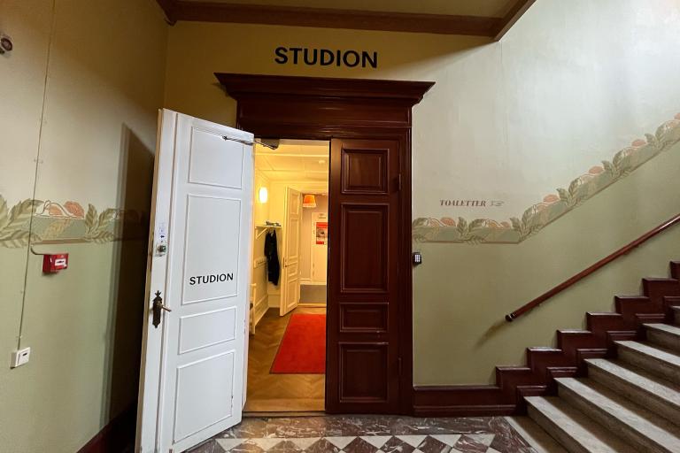 ingång Studions foajé. Bruna dörrar i trä, målade väggar grönt med bord av blad. Trappa till höger
