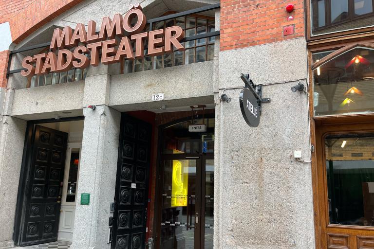 Ingång Kalendegatan 12c. Svart port, innanför glasdörrar. Ovanför en skylt med stora bokstäver, står Malmö Stadsteater i versaler. 