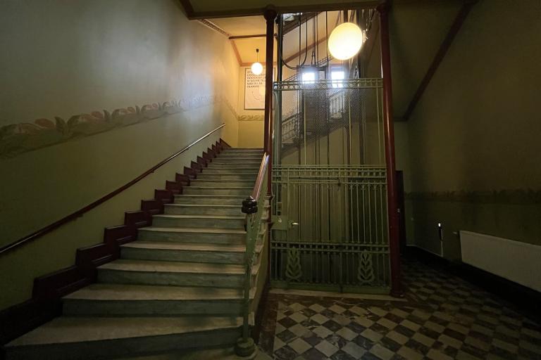Trapphuset Kalendegatan 12b. Rakt fram trappa och hiss. Gammalt trapphus med marmorgolv i schackrutor, målad bord längs med väggarna
