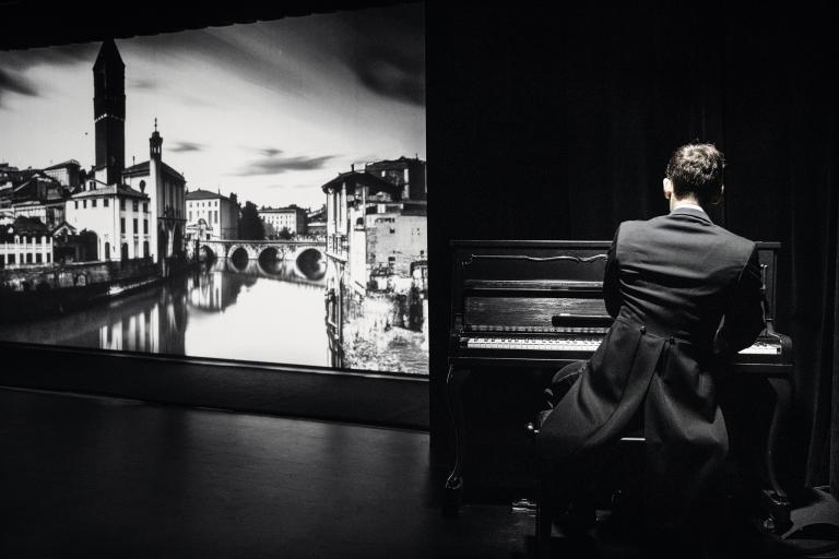 Pianist med ryggen mot publiken. Projektion av stad till vänster.