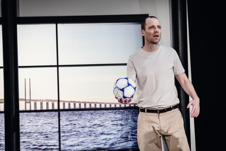 Man håller en fotboll framför ett fönster som visar Öresundsbron
