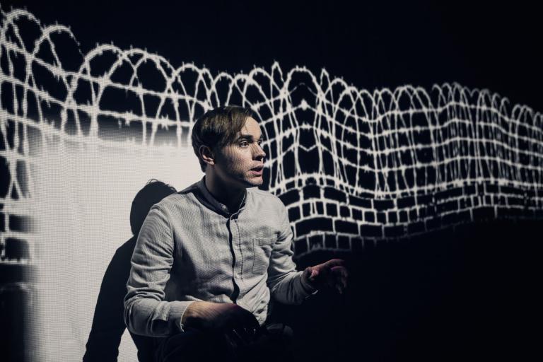 Föreställningsbild Stefan med projicerad taggtråd i bakgrunden
