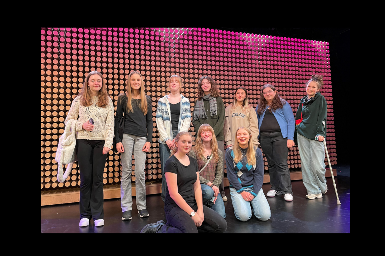 Gruppbild Lomma Kulturskola. Ungdomar står på scen mot en rosagul bakgrund