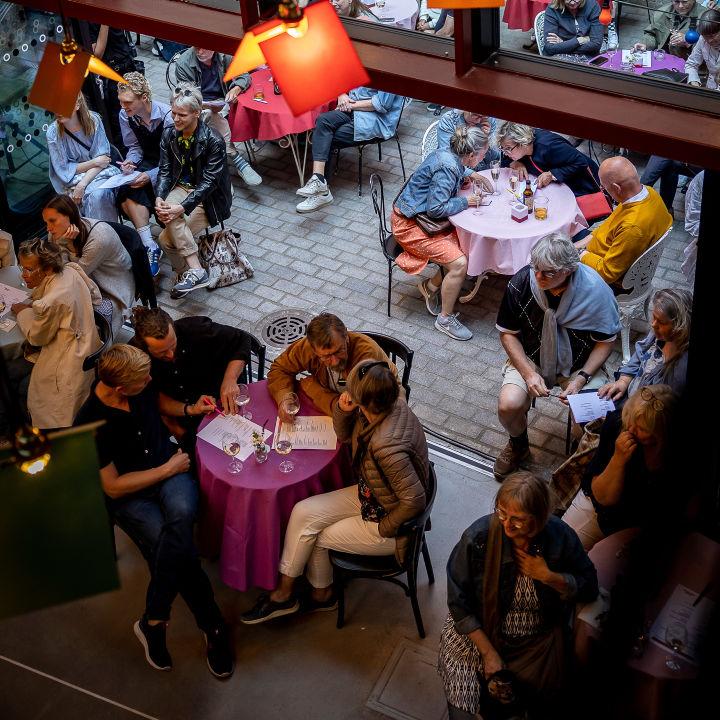 Jenny Baumgartner Bild ovanifrån på folk som sitter runt runda bord och pratar och dricker vin.