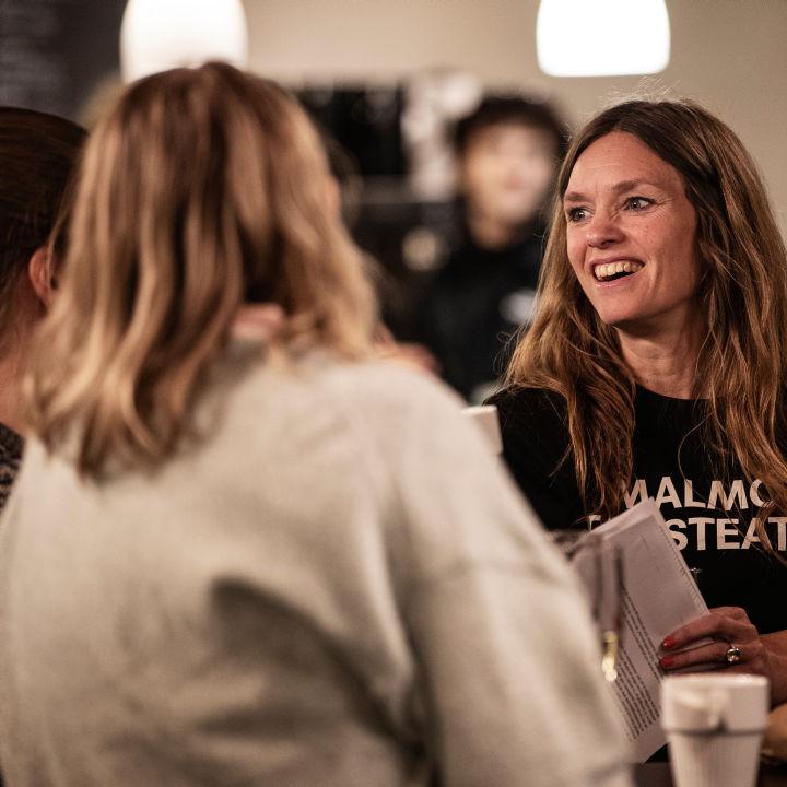 Emmalisa Pauly En person med Malmö Stadsteatertröja syns prata med två personer som har ryggen mot kameran.