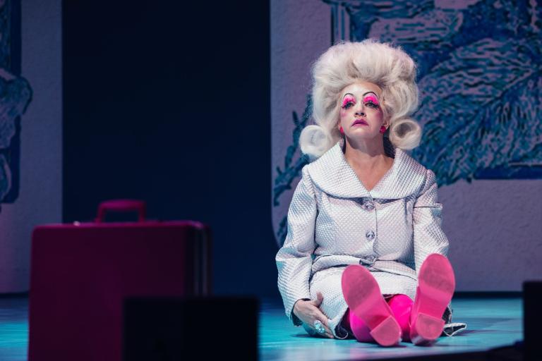 En barbie i mänsklig storlek sitter på golvet rak i ryggen. Vit stor frisyr