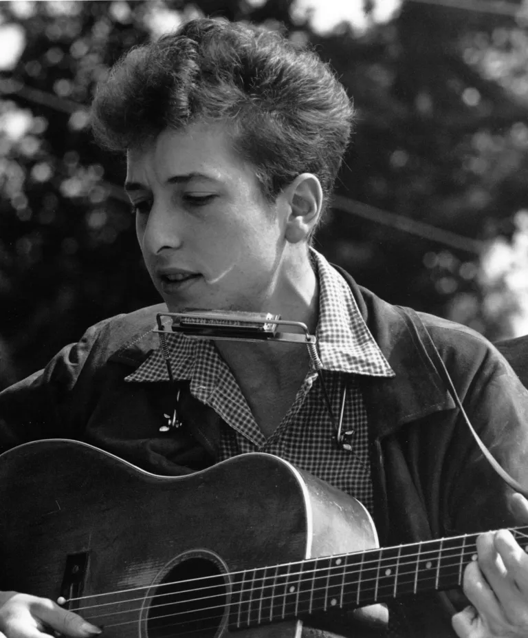 En ung Bob Dylan med akustisk gitarr och munspel 
