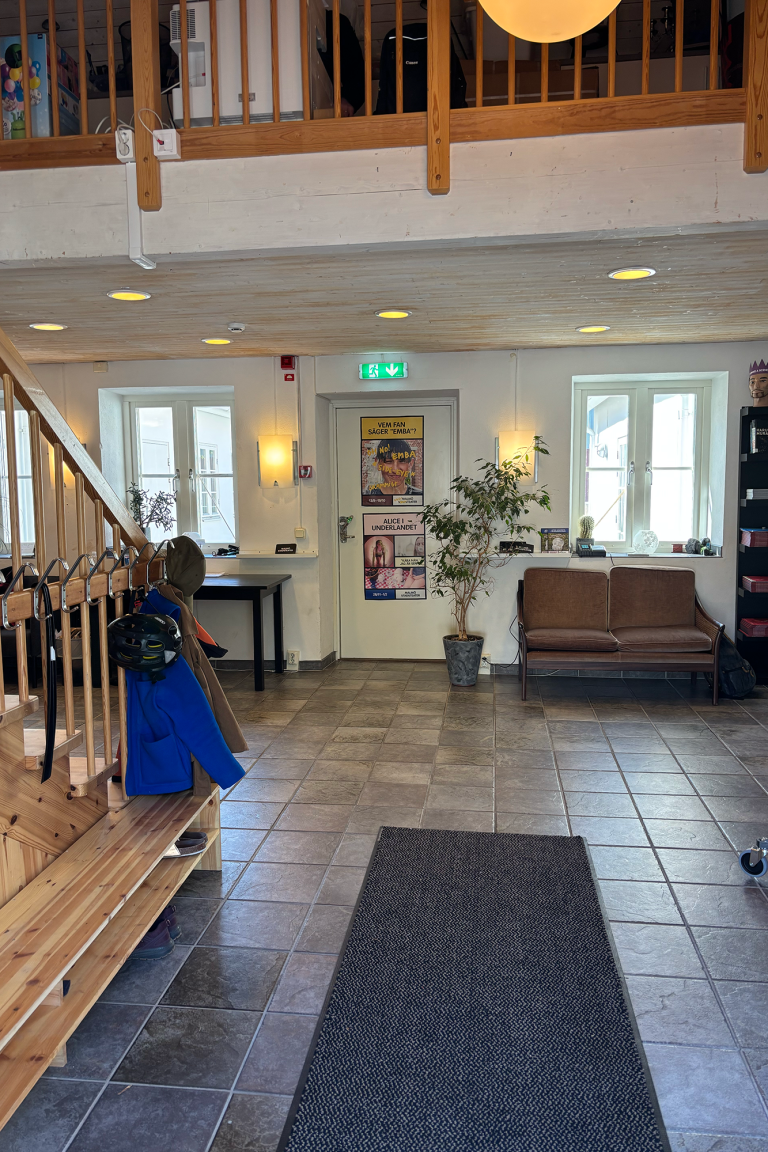 Malmö Stadsteater Entré med hängare till vänster och skohylla. Rakt fram en soffa och en växt. Bilder hänger på väggarna