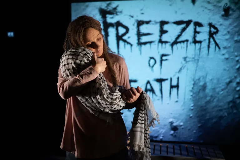 Kvinna håller ett bylte täckt av en svartvit keffiyeh (palestinasjal) framför texten "Freezer of Death".