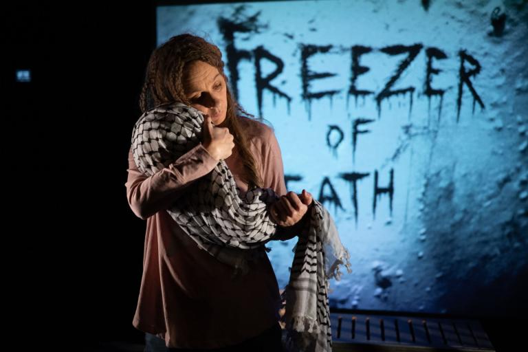 Kvinna håller ett bylte täckt av en svartvit keffiyeh (palestinasjal) framför texten "Freezer of Death".