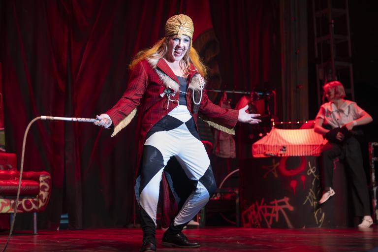 Sara P. Borgström Artist i röd kavaj och turban står i rampljuset med piska i handen likt en cirkusdirektör.