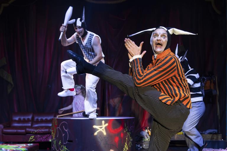 Sara P. Borgström Jyklare i randig tröja och mössa sparkar högt medan jonglör står bakom.