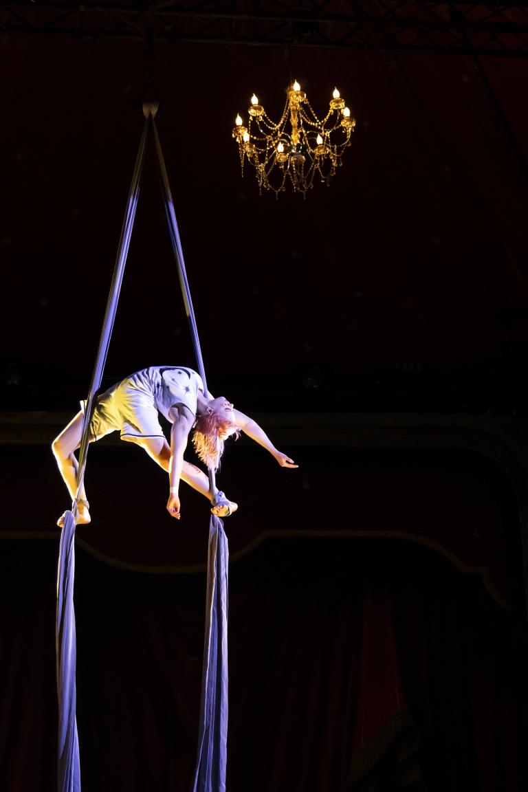 Sara P. Borgström Akrobat hänger upp och ner i tygband under en kristallkrona.