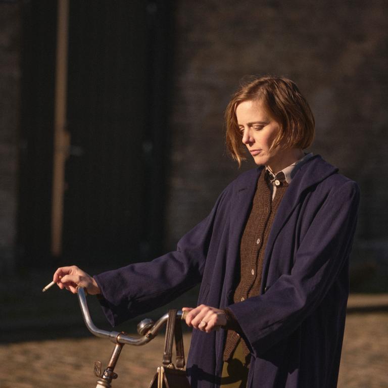 Kvinna står med en cykel. Cigarett i höger hand.